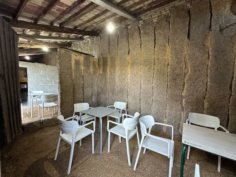 Mesas e cadeiras brancas baixo un alpendre de pedra